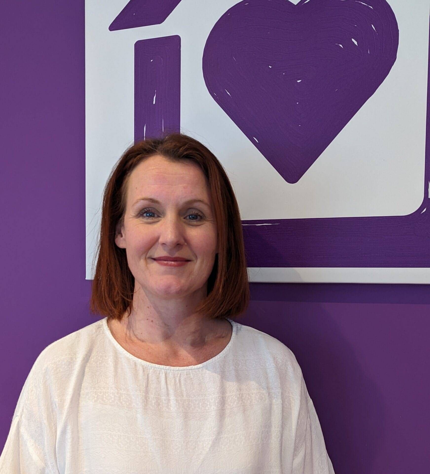 The Clinical Director of the Purple House Clinic Edinburgh standing in front of the Purple House Clinic logo, smiling.