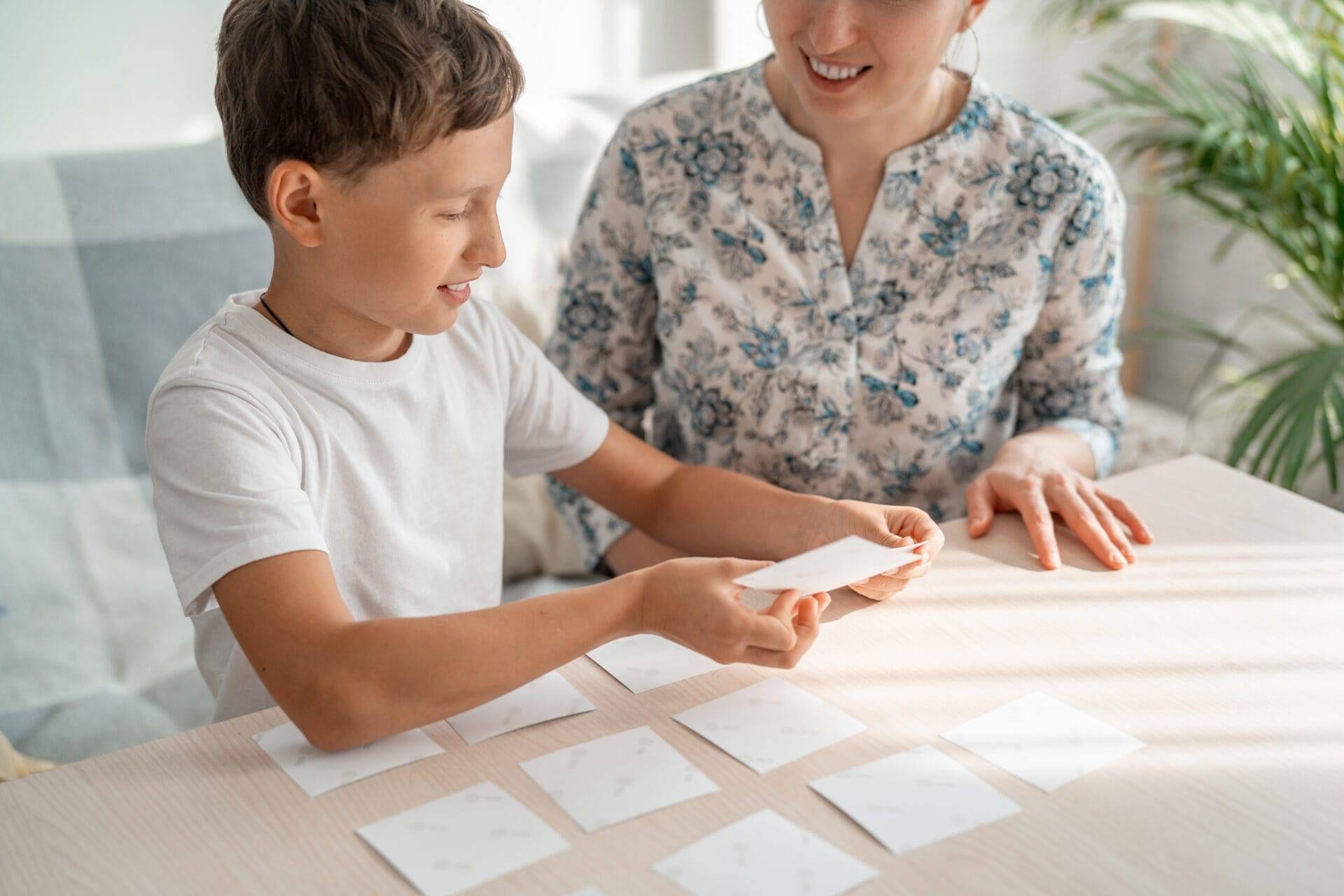 Smiling therapist and boy playing a memory card game together.