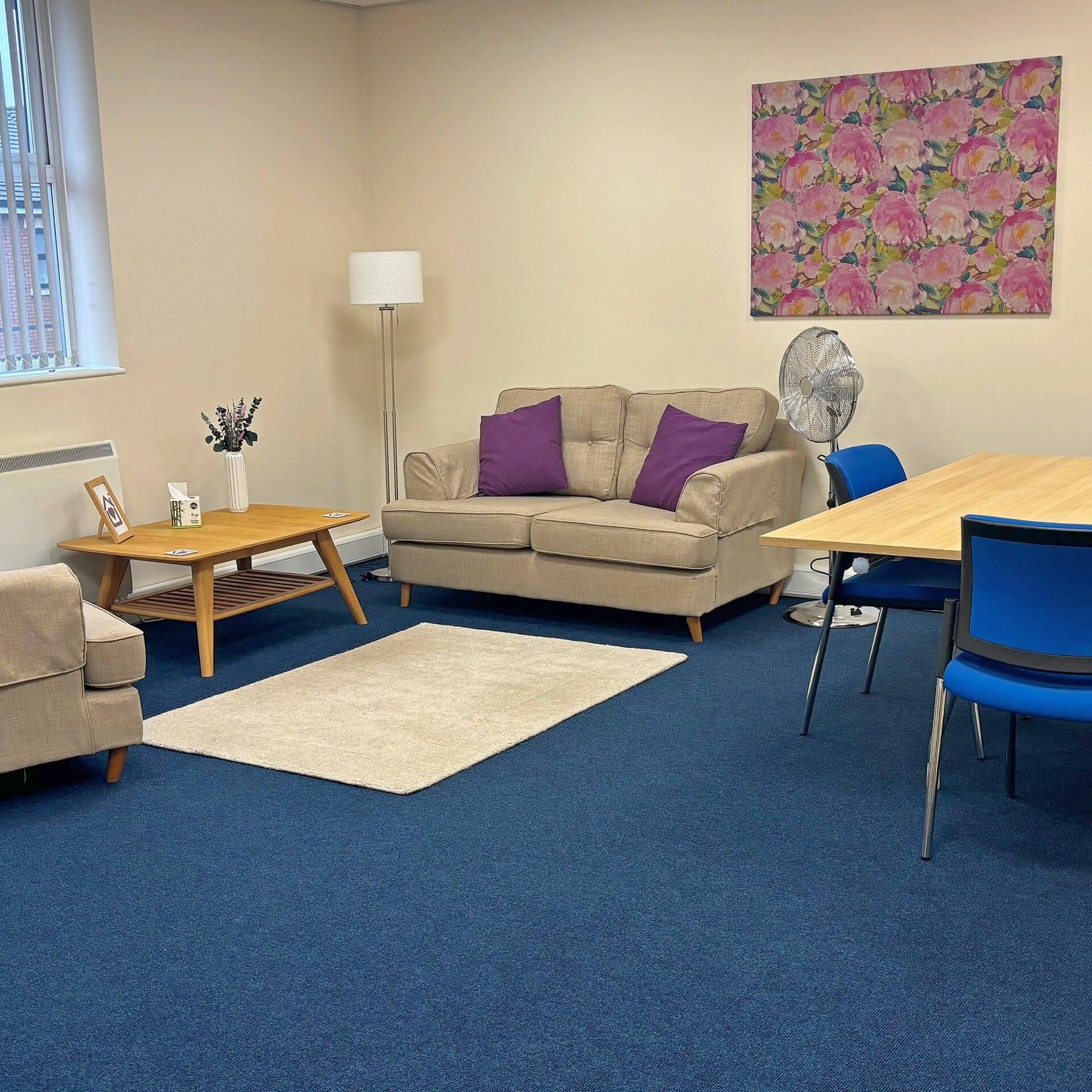 Therapy Room with comfortable sofa, coffee table, rug and wall hanging. A safe and homely setting for talking therapy at the Purple House Clinic Rugby