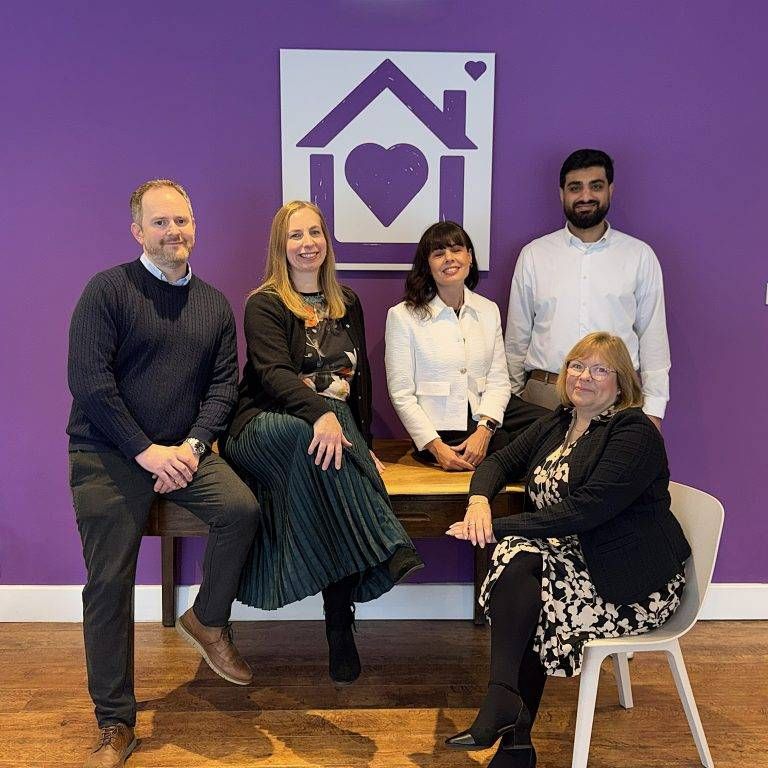 Five members of the Purple House Clinic Leicester team standing in front of a purple wall with the clinic's logo.