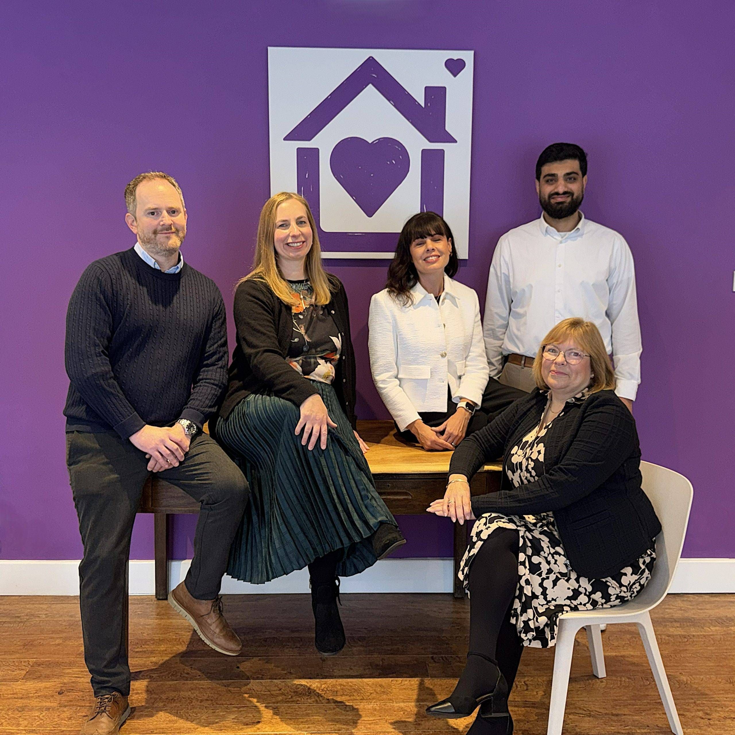 The Purple House Clinic Leicester | Mental Healthcare & Neurodiversity Clinic Five members of the Purple House Clinic Leicester team standing in front of a purple wall with the clinic's logo.
