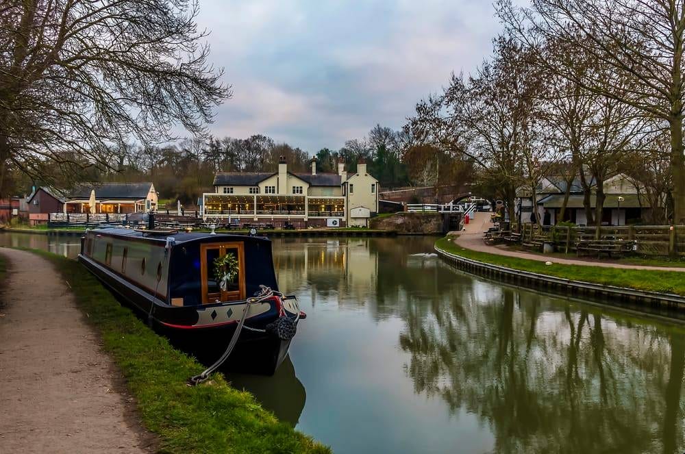 A view at dusk across the lower canal basin at Foxton Locks. A narrowboat and the Foxton Locks Inn are reflected in the still water on a winter's afternoon.