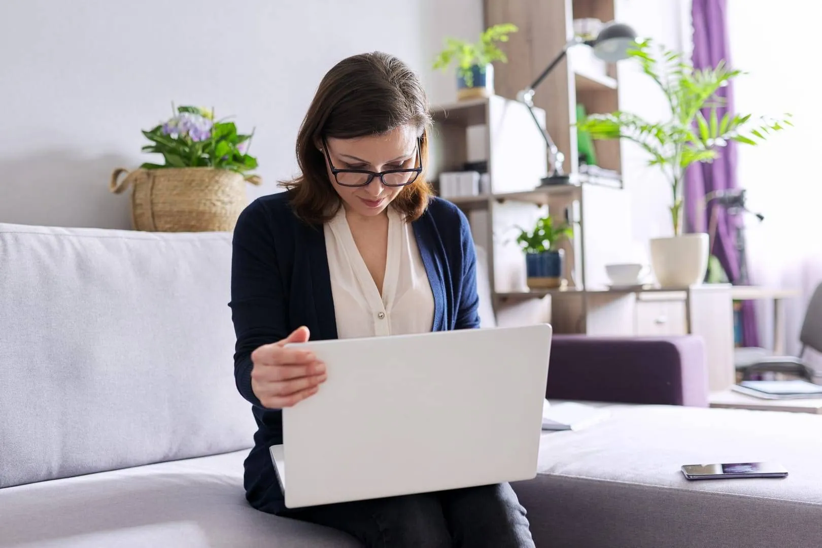 A person sitting on a sofa using a laptop, with plants in the background, illustrating a cozy online therapy session setup.