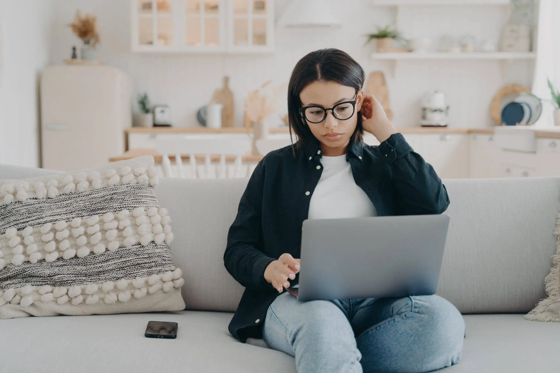 Woman with glasses using a laptop for online therapy while sitting cross-legged.