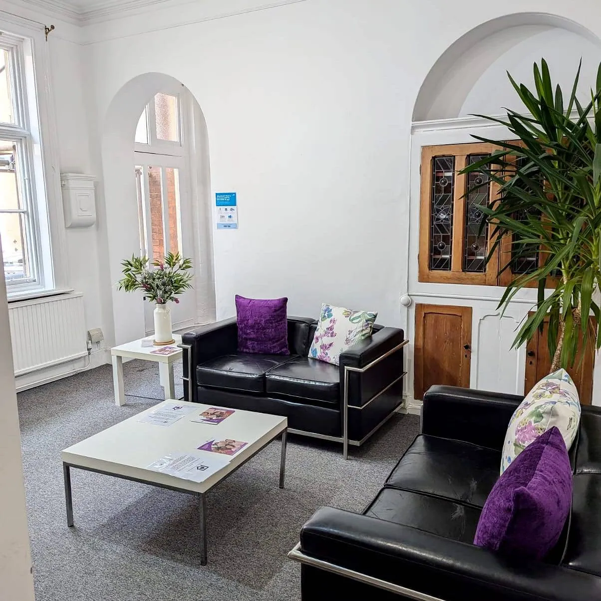 Beautiful therapy room with archways, two contemporary black leather sofas, coffee table and green plants. A safe and luxurious setting for psychological therapy sessions at the Purple House Clinic Nottingham.